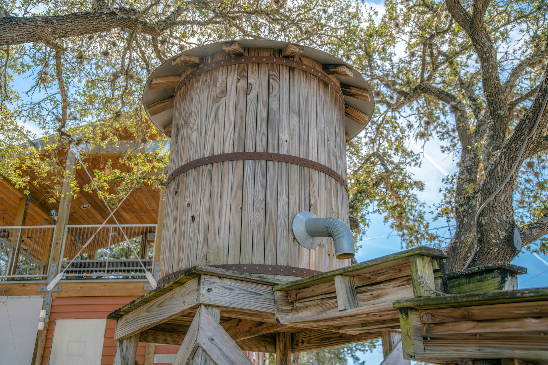 Vintage wooden water tank with pipe and waterway against trees and bright sky